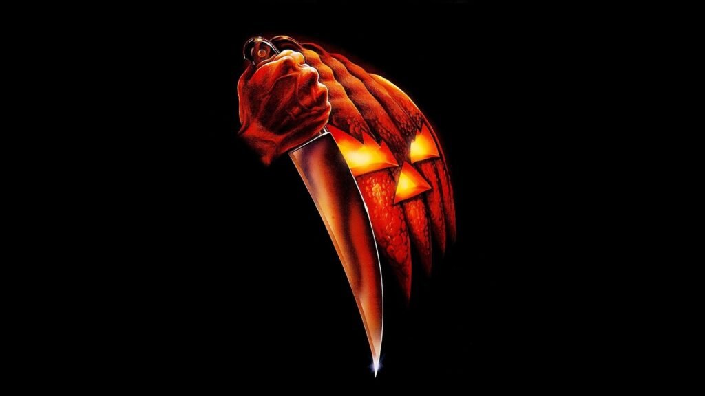 Official key art for Halloween (1978) — a hand gripping a butcher knife in front of a glowing jack-o'-lantern