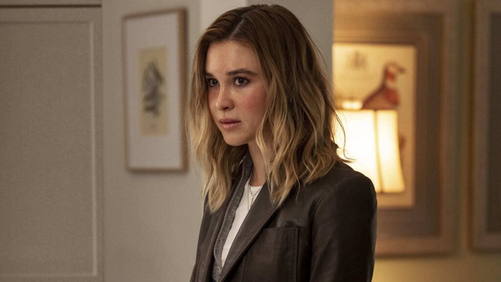 Isabel May as Tatum Evans in Scream 7, glancing warily over her shoulder in a lamplit room