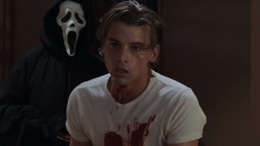 Ghostface standing behind a bloodied Billy Loomis (Skeet Ulrich) in Scream (1996)