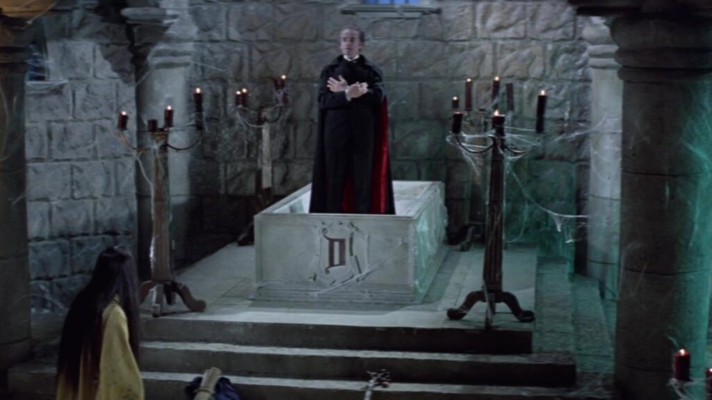 Count Dracula (John Forbes-Robertson) standing in his stone tomb in a candlelit crypt, the monk Kah kneeling before him, in The Legend of the 7 Golden Vampires (1974)