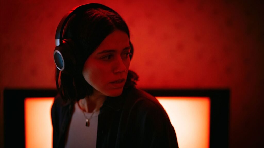 Nina Kiri as Evy Babic wearing headphones and listening in red light in Undertone (2026)
